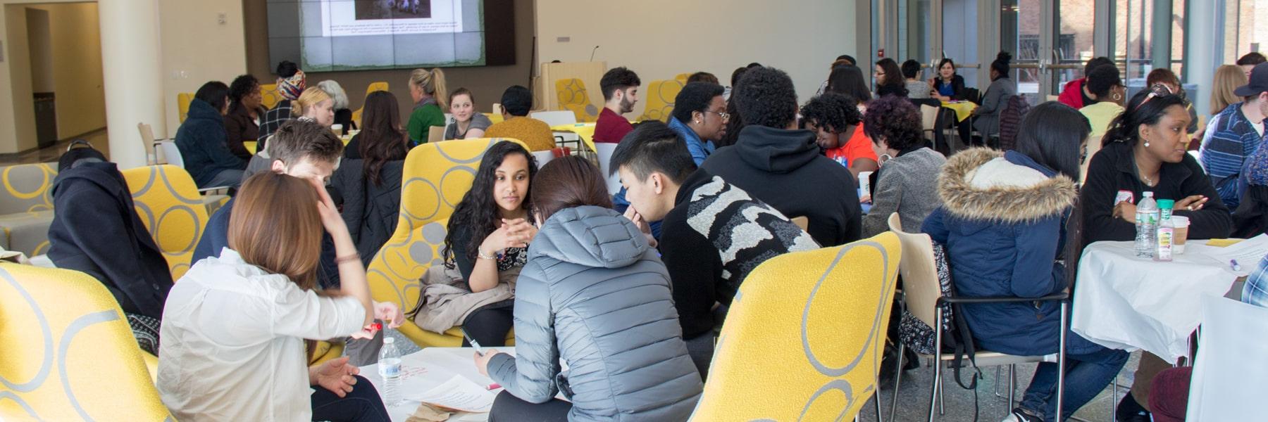 diverse students sitting around multiple tables having discussions